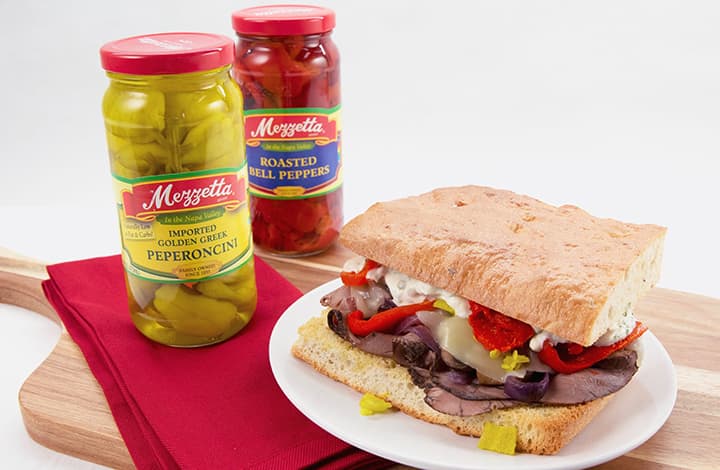 The Balboa aka the Italian Philly roast beef sandwich on cutting board with pepper jars